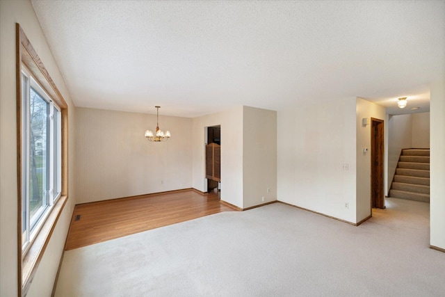 empty room with a textured ceiling, light colored carpet, baseboards, a chandelier, and stairs