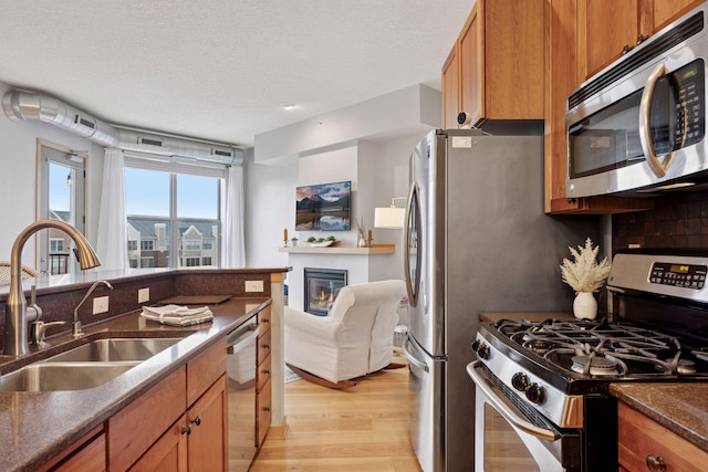 3640 Wooddale Ave S Unit 317, Saint Louis Park, MN 55416 - kitchen with stainless steel appliances, a sink, light wood-type flooring, brown cabinetry, and a glass covered fireplace