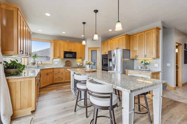kitchen with a kitchen island, tasteful backsplash, light stone countertops, black appliances, and light wood-style flooring