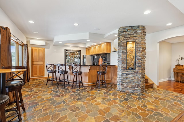 bar featuring stone flooring, wet bar, arched walkways, and a wall mounted air conditioner