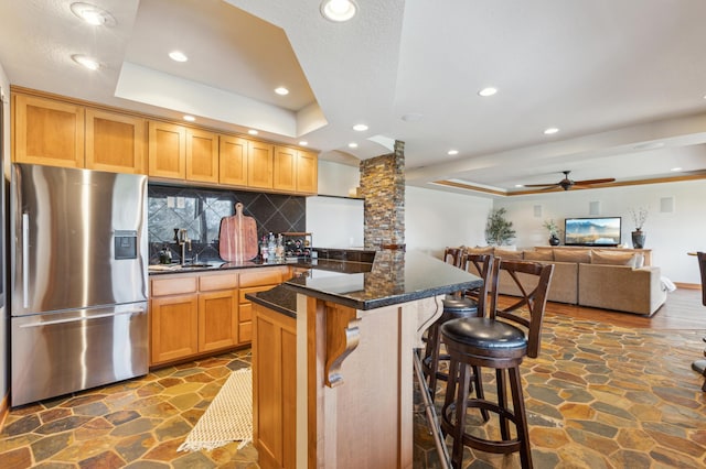 kitchen with stone floors, backsplash, a tray ceiling, and stainless steel refrigerator with ice dispenser