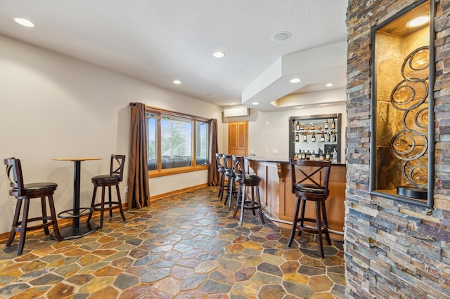 bar with stone flooring, a wall mounted air conditioner, recessed lighting, wet bar, and baseboards