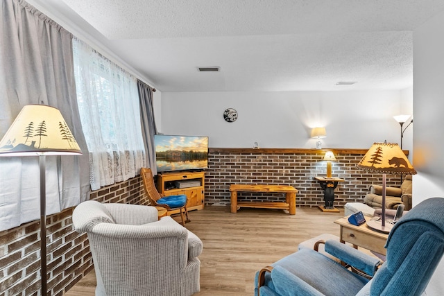 216 Richard Ave SE, Isanti, MN 55040 - living area featuring a textured ceiling, wood finished floors, and brick wall