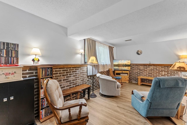 216 Richard Ave SE, Isanti, MN 55040 - living room featuring a textured ceiling, wainscoting, wood finished floors, a brick fireplace, and brick wall