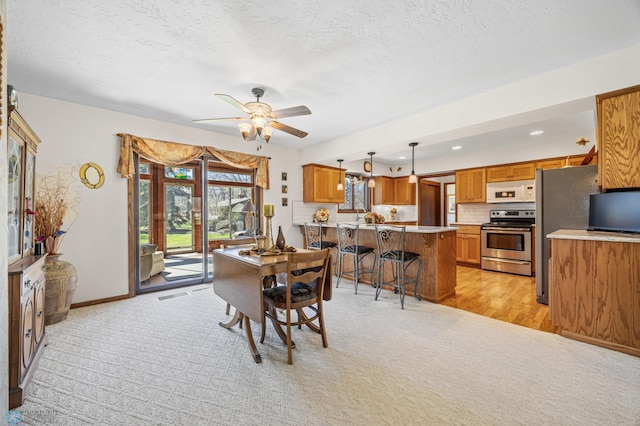 dining area with light colored carpet, a ceiling fan, baseboards, and a textured ceiling