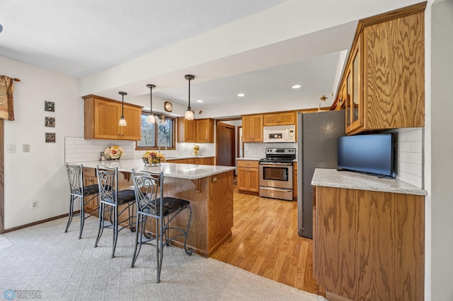 kitchen featuring a breakfast bar area, stainless steel appliances, brown cabinetry, and a peninsula