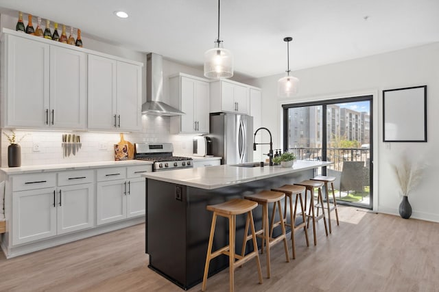 kitchen with a sink, light wood-style floors, wall chimney exhaust hood, stainless steel appliances, and tasteful backsplash