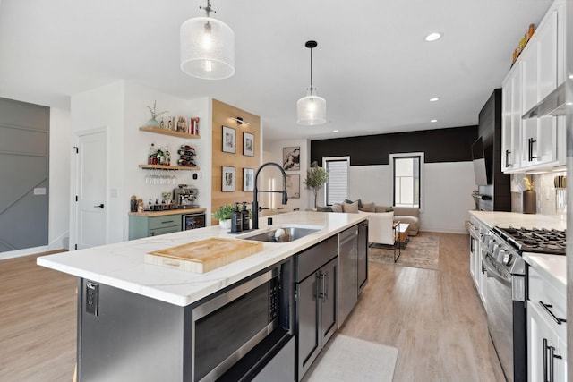 kitchen with appliances with stainless steel finishes, a sink, a kitchen island with sink, white cabinetry, and decorative light fixtures