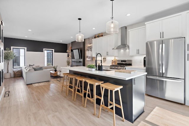 kitchen with wall chimney range hood, a sink, a kitchen breakfast bar, stainless steel appliances, and open floor plan