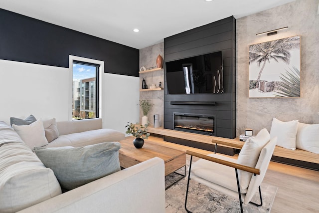 living area with recessed lighting, an accent wall, wood finished floors, and a fireplace