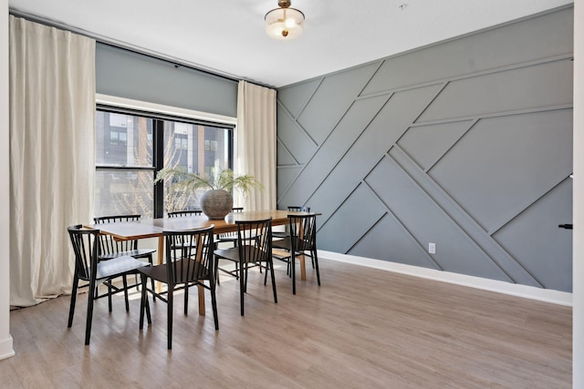 dining space featuring light wood-style floors, baseboards, and a decorative wall