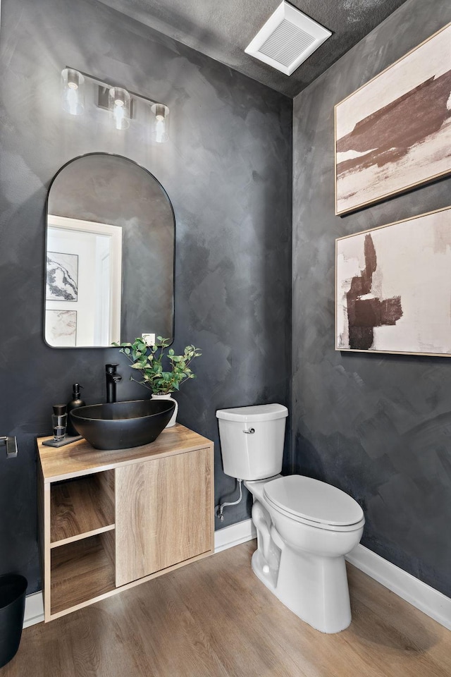 half bathroom featuring visible vents, wood finished floors, vanity, baseboards, and toilet