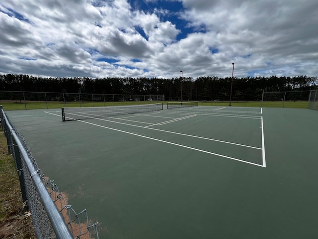 view of tennis court featuring community basketball court, fence, and a view of trees
