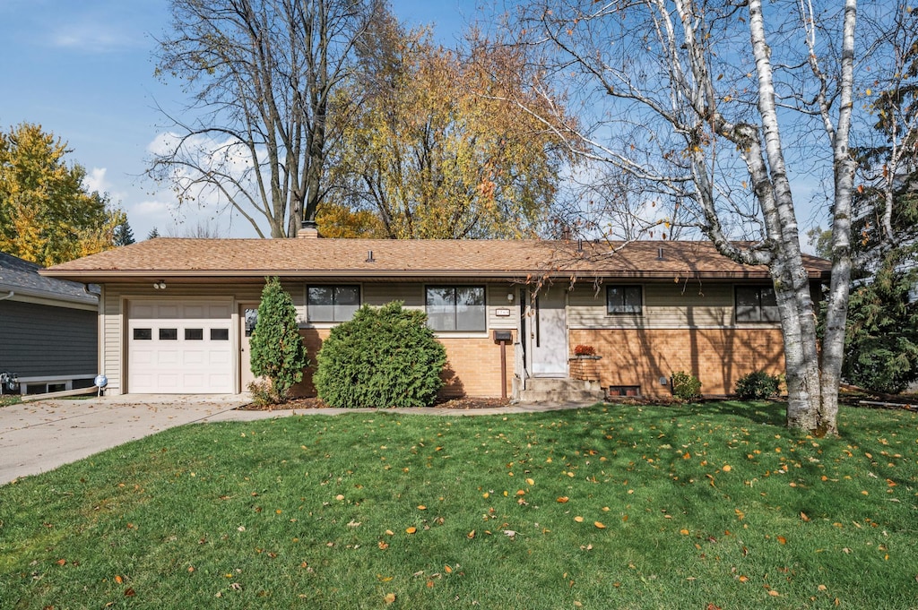 ranch-style house featuring a chimney, a front yard, a garage, brick siding, and concrete driveway