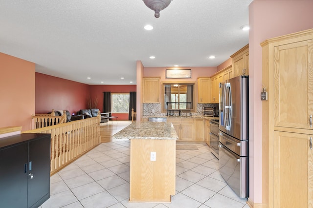 kitchen featuring light brown cabinetry, light stone countertops, open floor plan, a center island, and appliances with stainless steel finishes