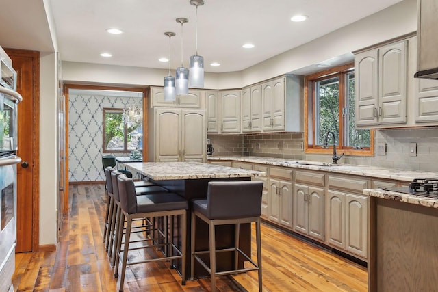 1055 Nelson Dr, Shoreview, MN 55126 - kitchen with a kitchen bar, light wood-type flooring, hanging light fixtures, a sink, and light stone counters