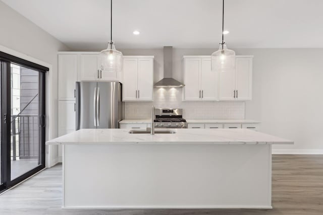 kitchen featuring wall chimney range hood, a sink, stainless steel appliances, white cabinetry, and backsplash