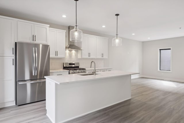 kitchen featuring wall chimney range hood, appliances with stainless steel finishes, a sink, and light wood finished floors