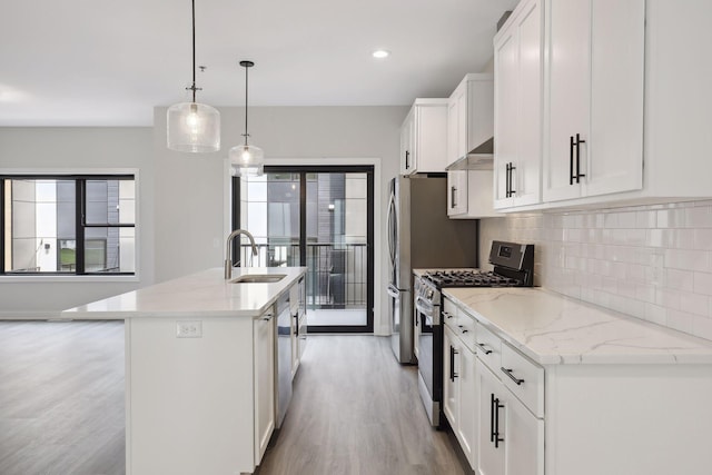 kitchen featuring a kitchen island with sink, white cabinetry, a sink, light wood-style flooring, and appliances with stainless steel finishes
