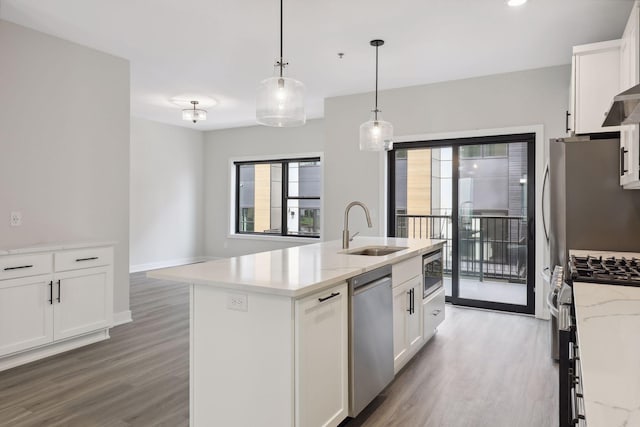 kitchen with a kitchen island with sink, white cabinetry, a sink, light wood finished floors, and stainless steel appliances