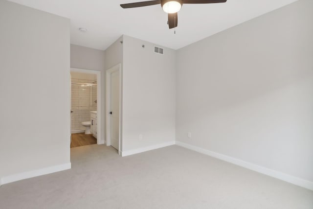 unfurnished bedroom featuring ceiling fan, light colored carpet, baseboards, ensuite bathroom, and visible vents