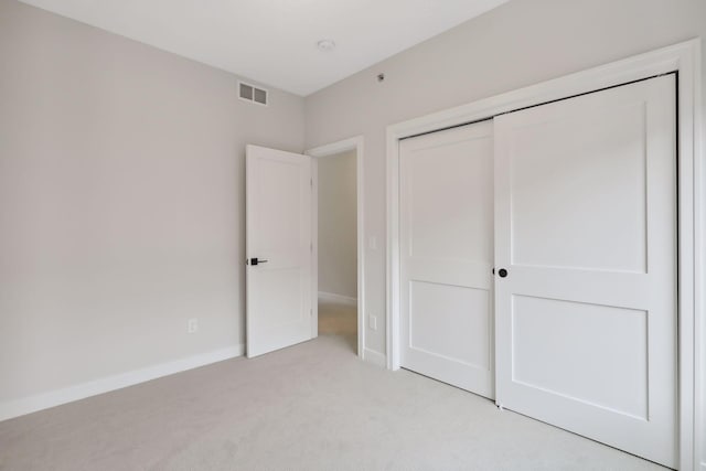 unfurnished bedroom with a closet, baseboards, light colored carpet, and visible vents