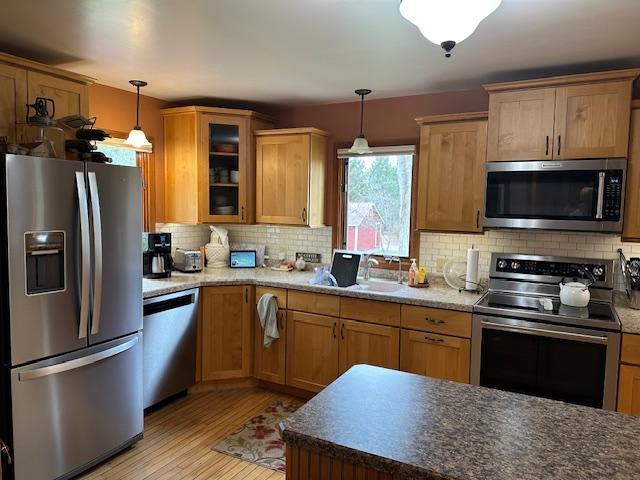 9700 Aspen Ave NW, Bemidji, MN 56601 - kitchen with light wood finished floors, stainless steel appliances, decorative light fixtures, backsplash, and glass insert cabinets