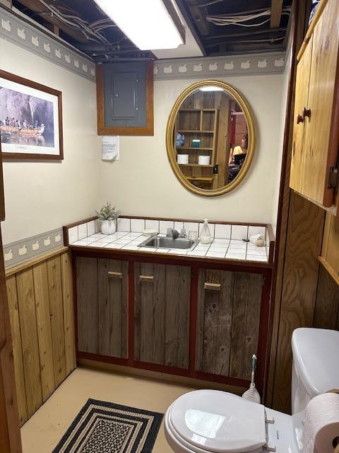 9700 Aspen Ave NW, Bemidji, MN 56601 - half bath featuring vanity, wood walls, toilet, a wainscoted wall, and finished concrete floors