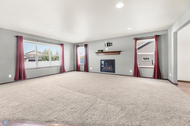 unfurnished living room with a glass covered fireplace, baseboards, carpet flooring, and recessed lighting