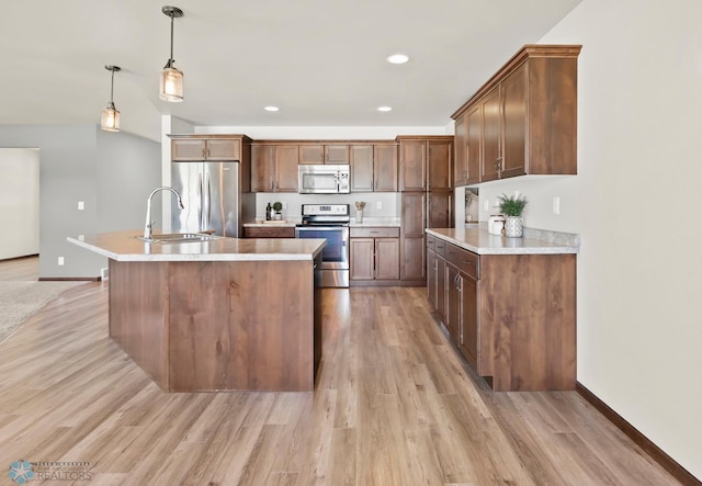 kitchen with appliances with stainless steel finishes, a sink, light wood-type flooring, light countertops, and a kitchen island with sink