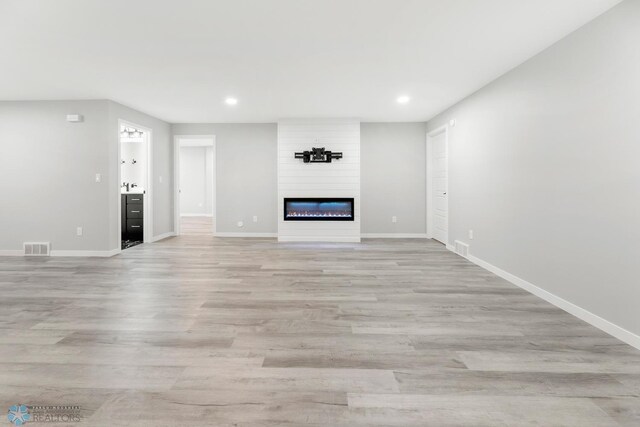 unfurnished living room featuring baseboards, recessed lighting, light wood-type flooring, and a large fireplace