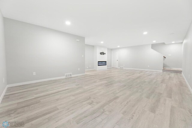 below grade area with light wood finished floors, baseboards, recessed lighting, stairway, and a large fireplace