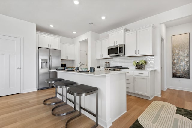 kitchen with stainless steel appliances, light wood finished floors, white cabinetry, a kitchen island with sink, and recessed lighting