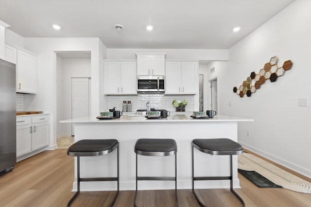 kitchen with stainless steel appliances, a kitchen bar, backsplash, white cabinets, and light wood-style floors