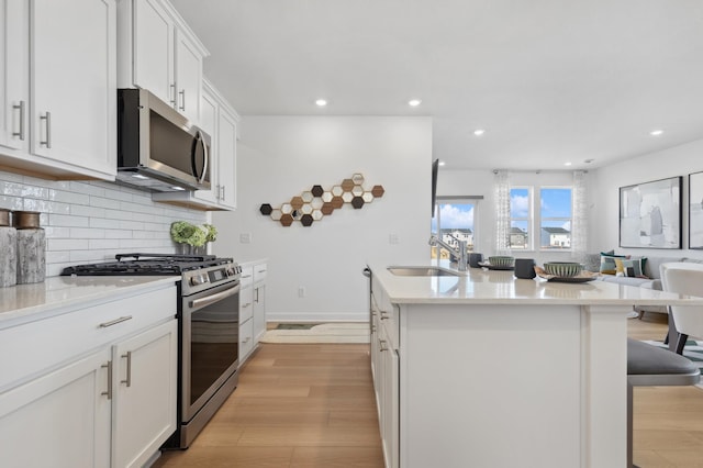 kitchen featuring stainless steel appliances, a sink, light wood-style floors, a center island with sink, and decorative backsplash