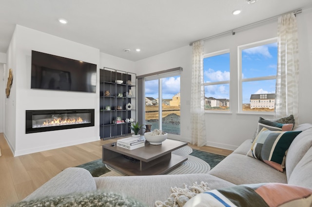 living room featuring wood finished floors, a glass covered fireplace, recessed lighting, and baseboards
