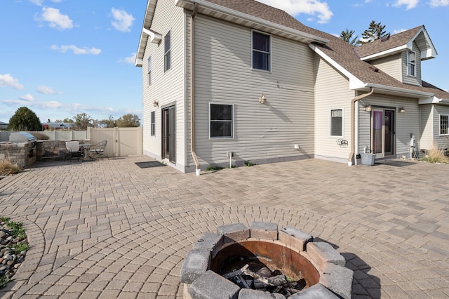 rear view of house featuring roof with shingles, fence, a fire pit, and a patio area