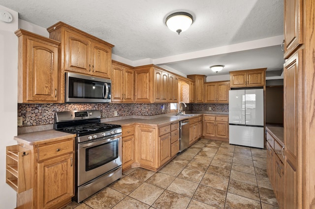 kitchen featuring brown cabinets, appliances with stainless steel finishes, a sink, a textured ceiling, and decorative backsplash