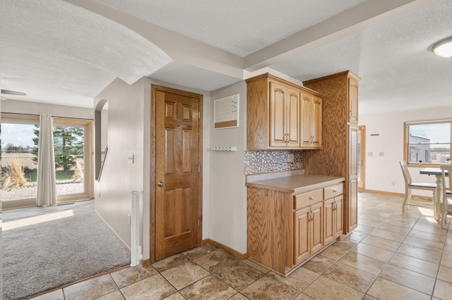 kitchen with light countertops, arched walkways, a textured ceiling, baseboards, and tasteful backsplash