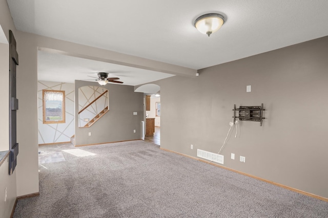 unfurnished room with visible vents, baseboards, ceiling fan, arched walkways, and carpet flooring