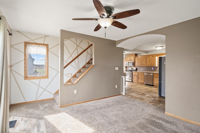 unfurnished living room featuring ceiling fan, arched walkways, stairway, baseboards, and light carpet