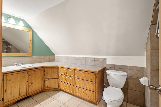 bathroom featuring tile walls, vaulted ceiling, vanity, tile patterned floors, and toilet