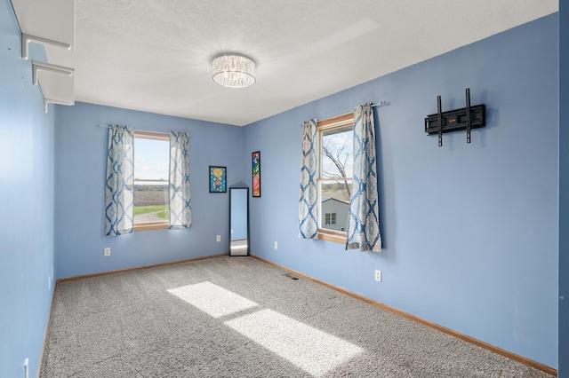 carpeted spare room featuring a chandelier, baseboards, and visible vents