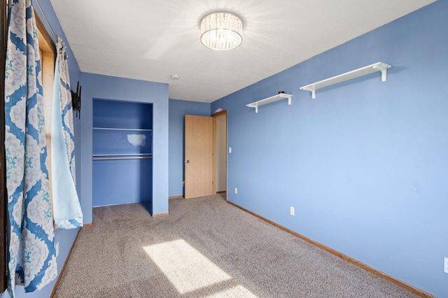 unfurnished bedroom featuring carpet floors, baseboards, a notable chandelier, and a closet