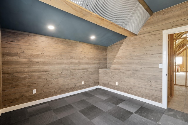 empty room featuring baseboards, wood walls, and lofted ceiling