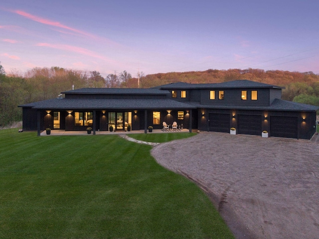 view of front of home with gravel driveway, a patio, a front lawn, and an attached garage