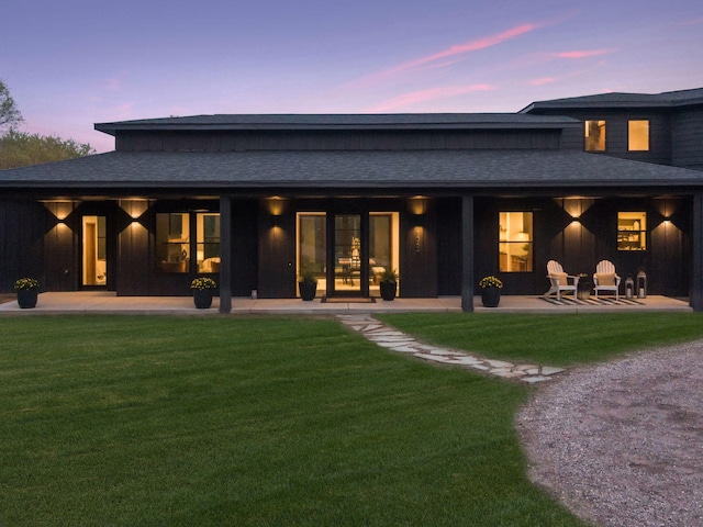 back of property at dusk with a yard, a patio, and a shingled roof