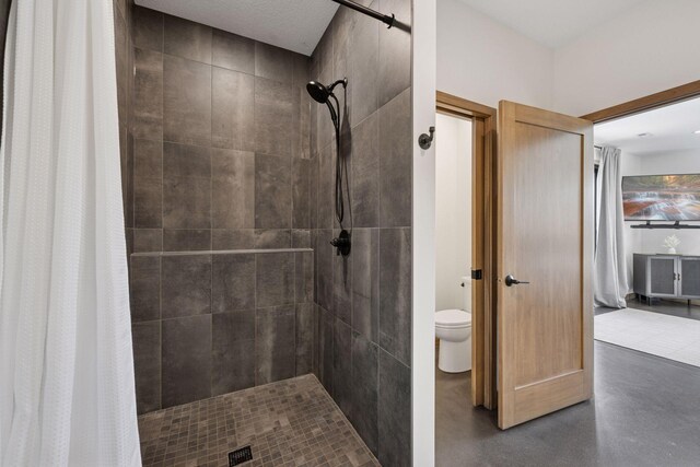 bathroom with a tile shower, toilet, and finished concrete floors