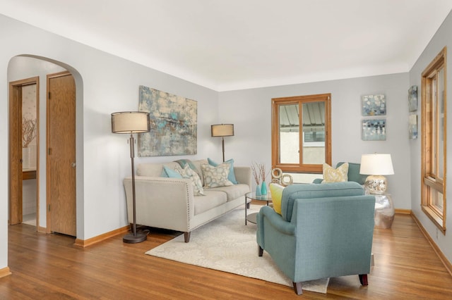 living area featuring baseboards, arched walkways, and wood finished floors
