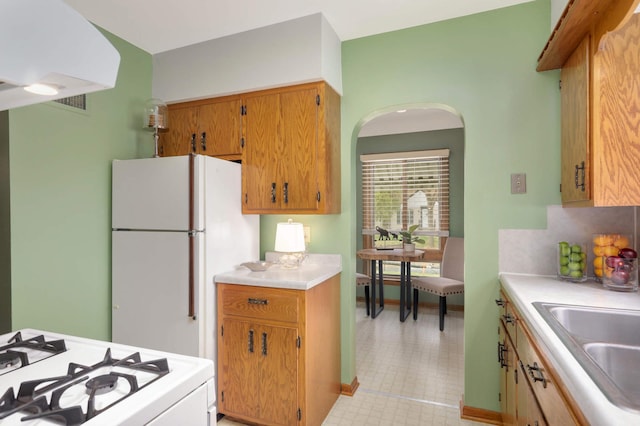 kitchen with white appliances, light countertops, arched walkways, brown cabinets, and a sink
